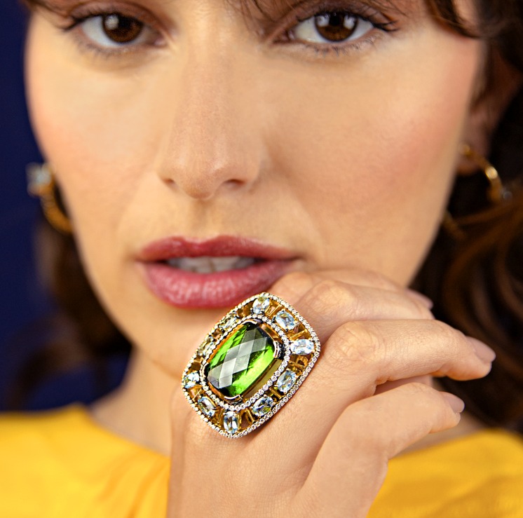 Na foto, o anel em ouro amarelo com turmalina verde emoldurada por águas marinha e diamantes brancos da Coleção Marine